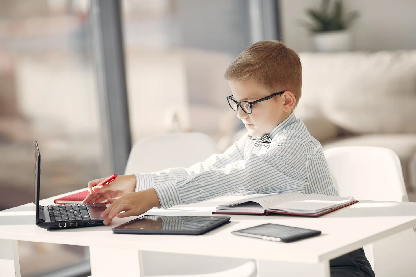 A child wearing glasses and a bow tie plays entrepreneur at a desk with a laptop.